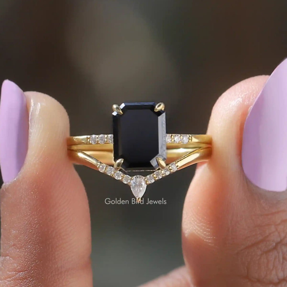 Two fingers holding the Black Emerald Cut Moissanite Bridal Ring Set