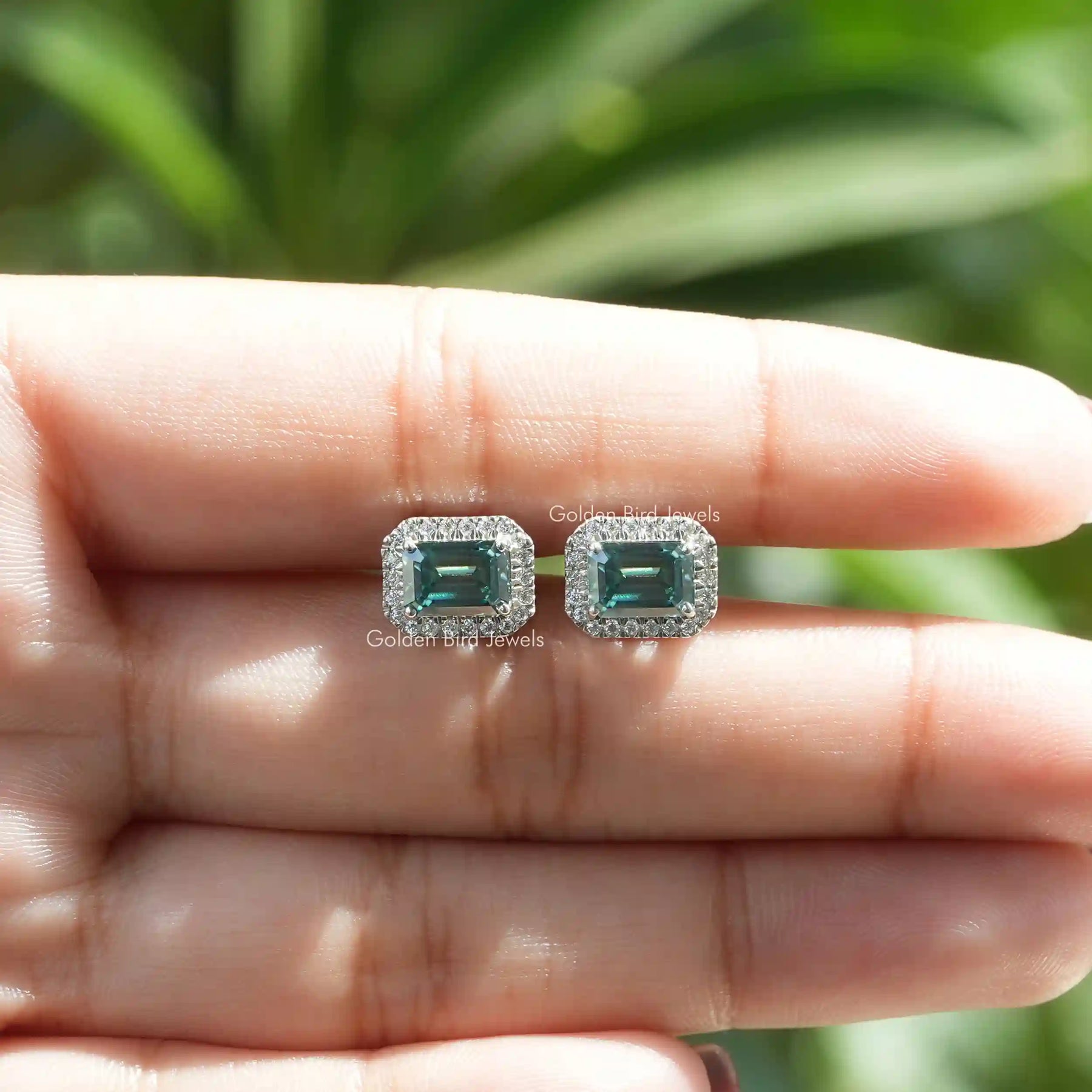 In a two-finger view of earrings in green emerald cut moissanite