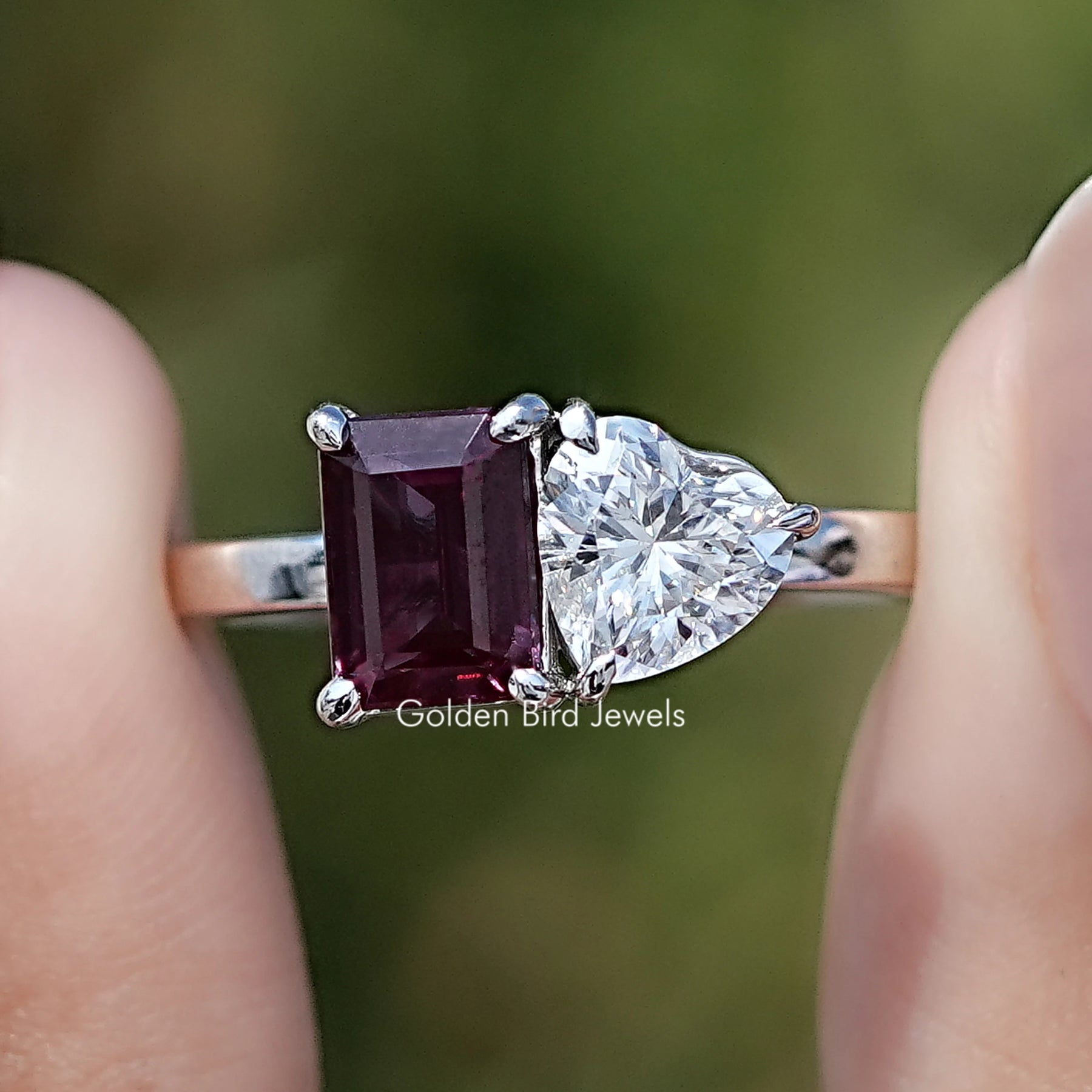 Front view of Alexandrite Gemstone And Heart Moissanite Toi Et Moi Ring in two fingers