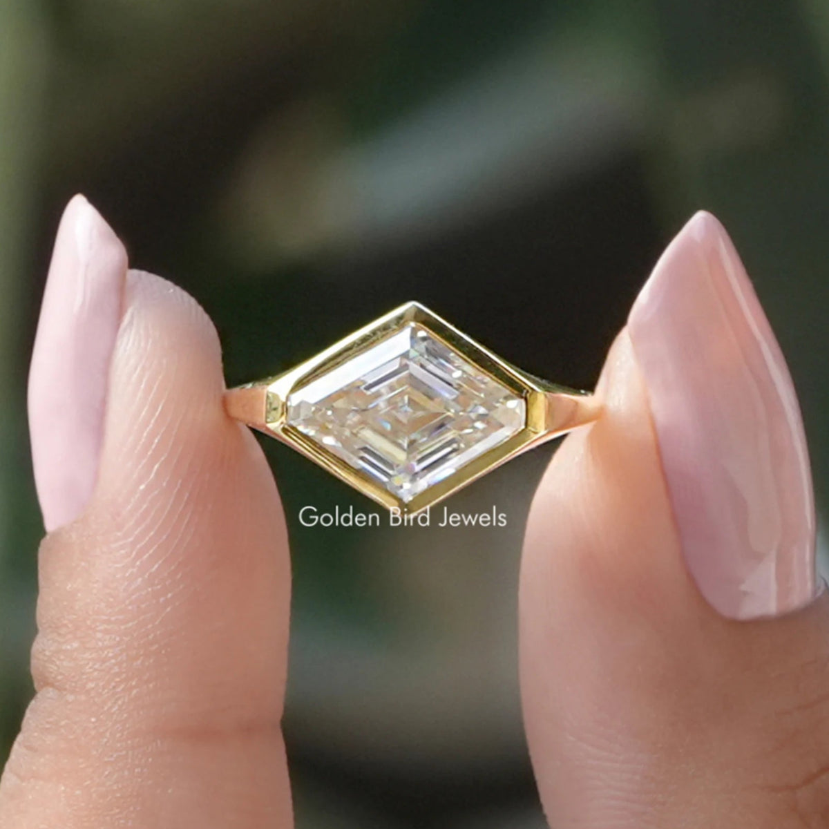 Two fingers holding the Lozenge Cut Moissanite Bezel Set Solitaire Ring