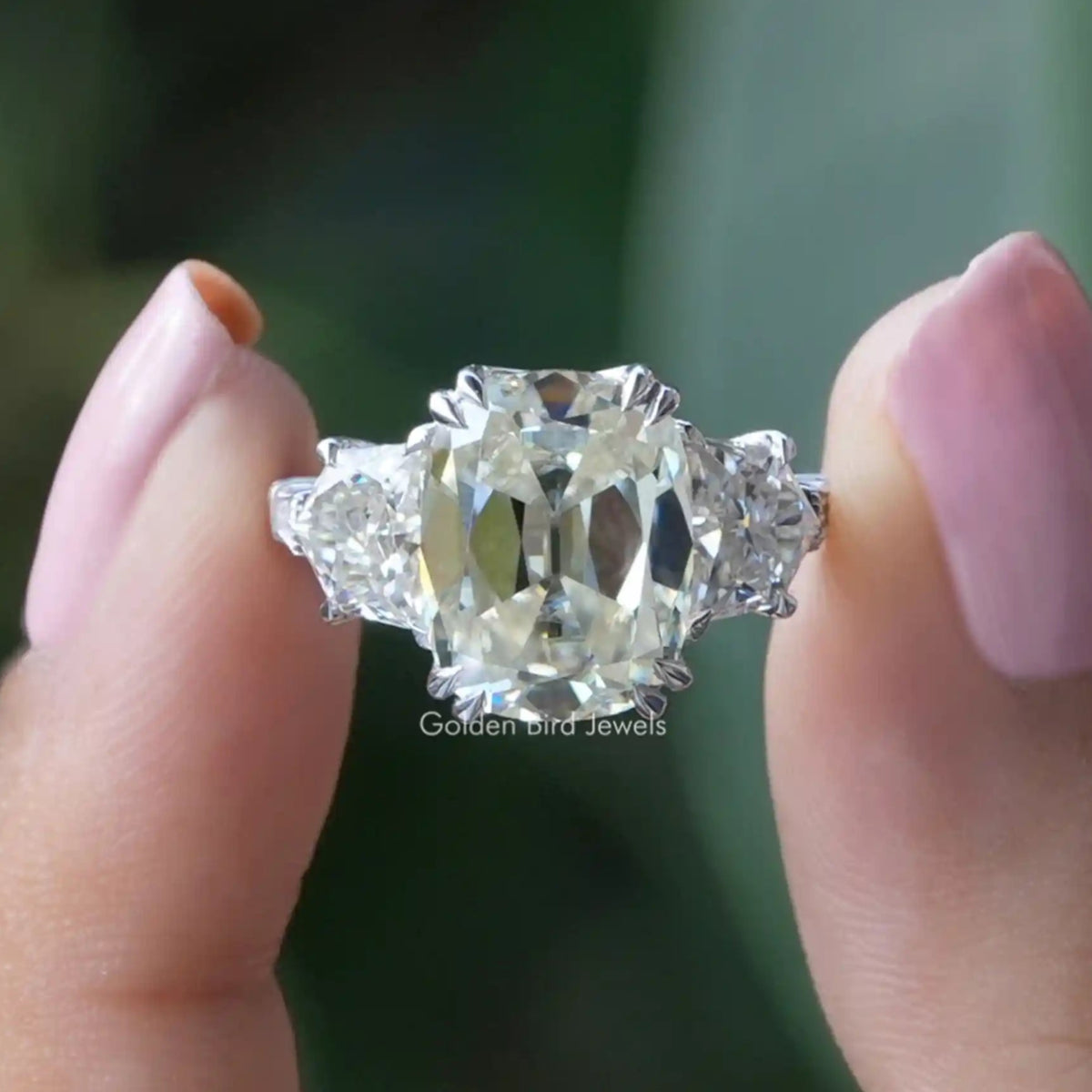 Two fingers holding the Old Mine Cushion Cut Three Stone Moissanite Ring