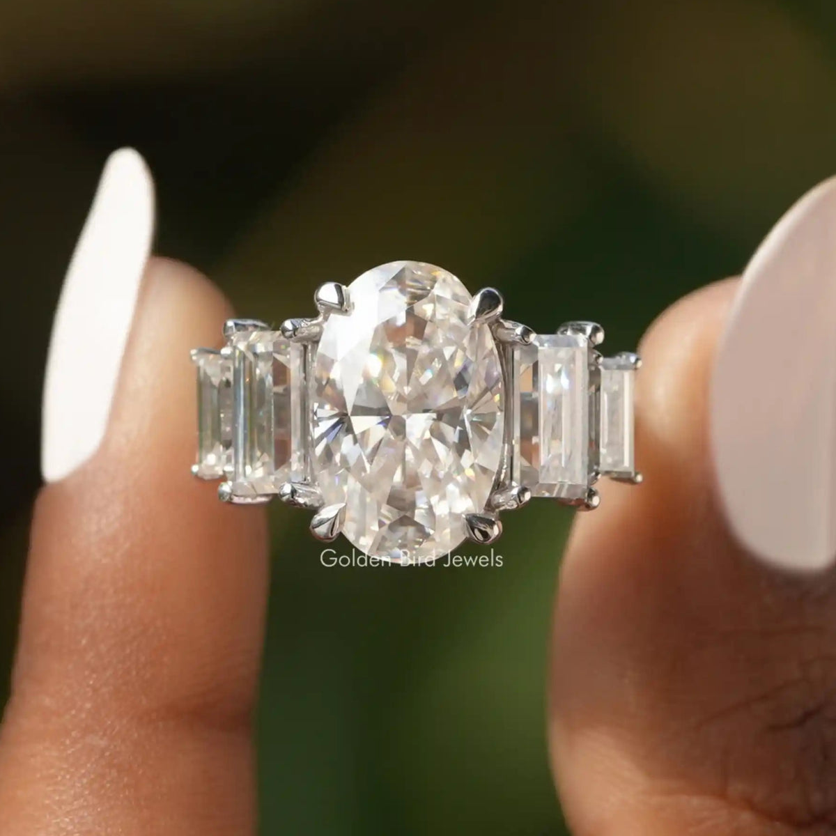 Front view of Crushed Ice Oval And Baguette Cut Moissanite Five Stone Ring in two fingers