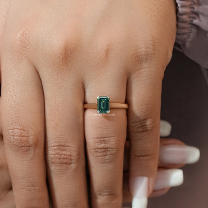 Emerald-cut moissanite ring on finger with dark green center stone and thin band