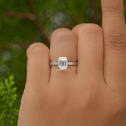 Emerald-cut moissanite bezel-set engagement ring on hand, front view of the stone