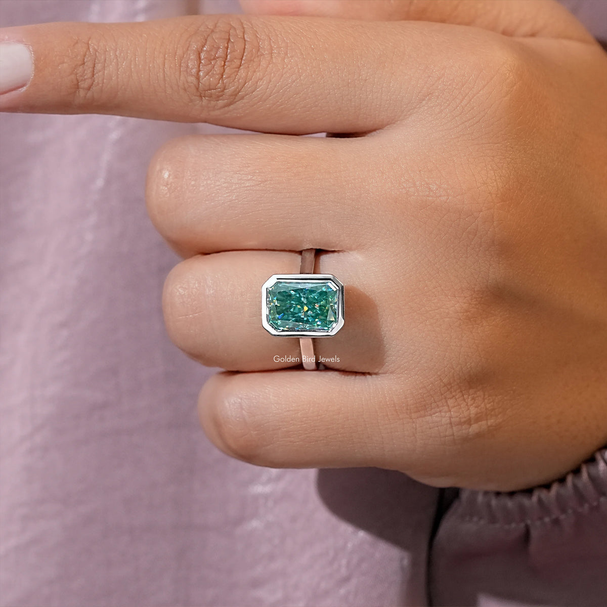 Teal moissanite solitaire ring close-up on fingertip, emerald-cut bezel