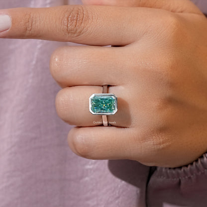 Teal moissanite solitaire ring close-up on fingertip, emerald-cut bezel