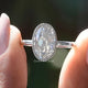 Two fingers holding the Oval Cut Bezel Set Moissanite Engagement Ring
