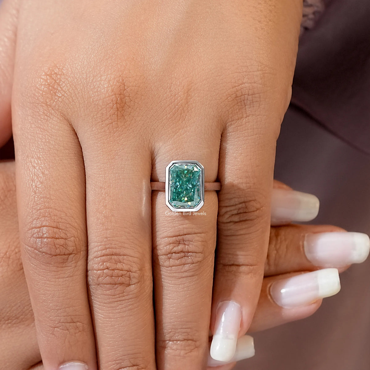 Teal emerald-cut moissanite solitaire ring on hand, bezel-set center stone