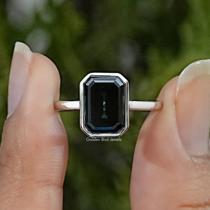 Emerald-cut moissanite solitaire ring with a dark rectangular stone in a silver bezel setting