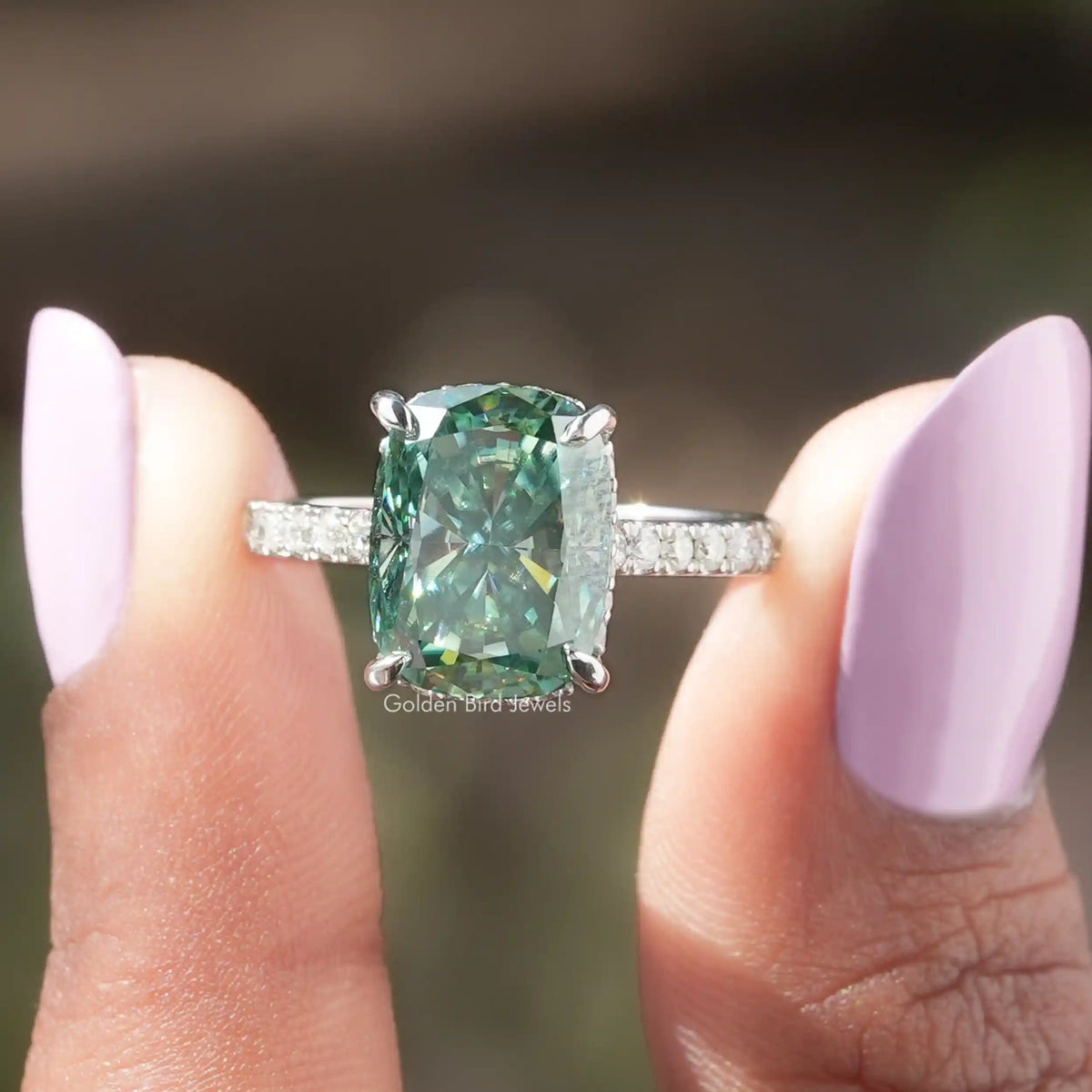 Two fingers holding the Green Cushion Cut Moissanite Hidden Halo Ring