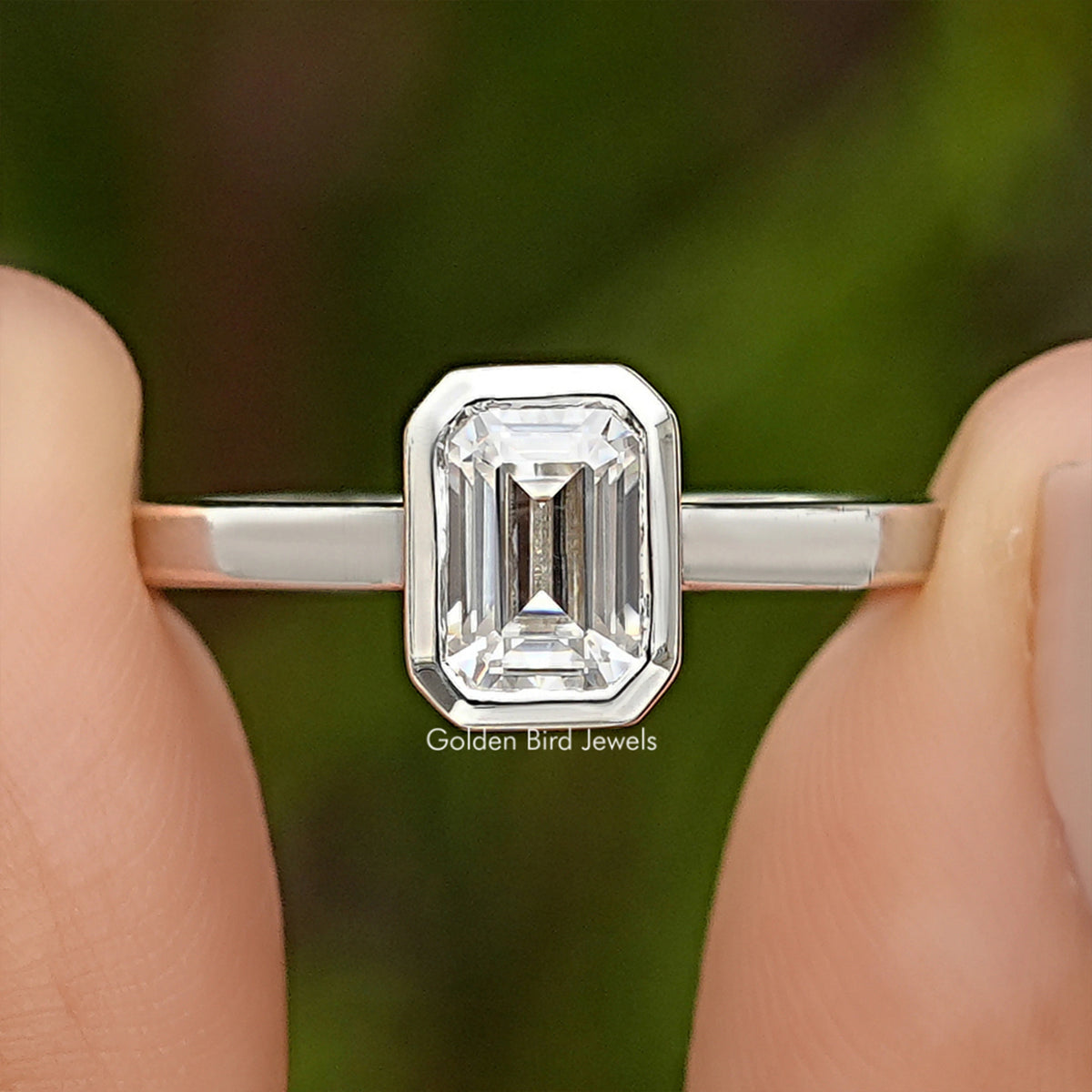 Bezel-set emerald-cut moissanite engagement ring in silver, square center stone close-up