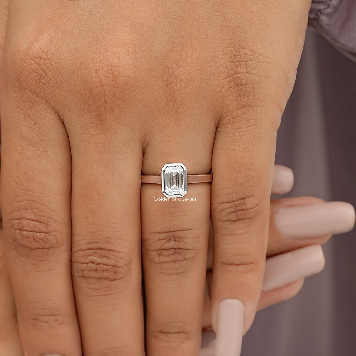 Emerald-cut moissanite bezel-set engagement ring on hand, front view with bezel setting