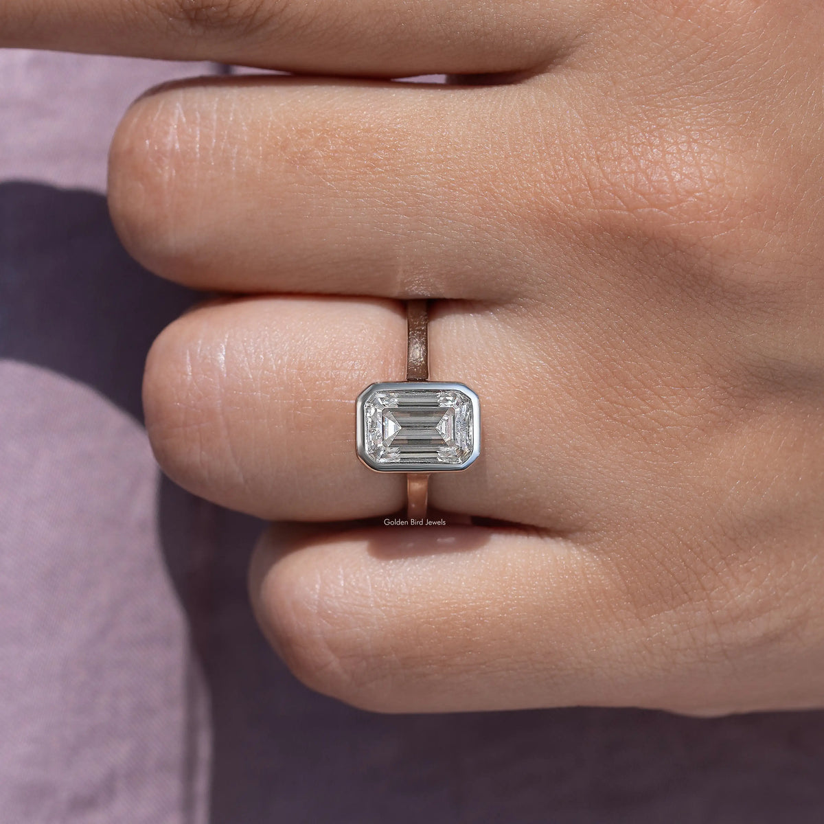 Emerald-cut moissanite bezel-set solitaire ring in close-up on hand