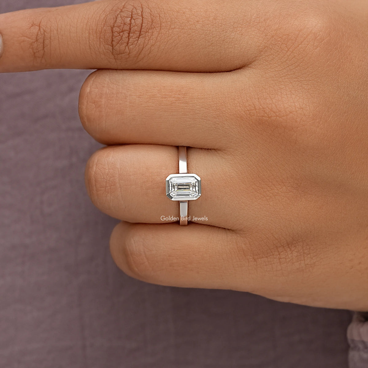 Close-up of emerald-cut moissanite bezel-set ring on fingers, square center stone