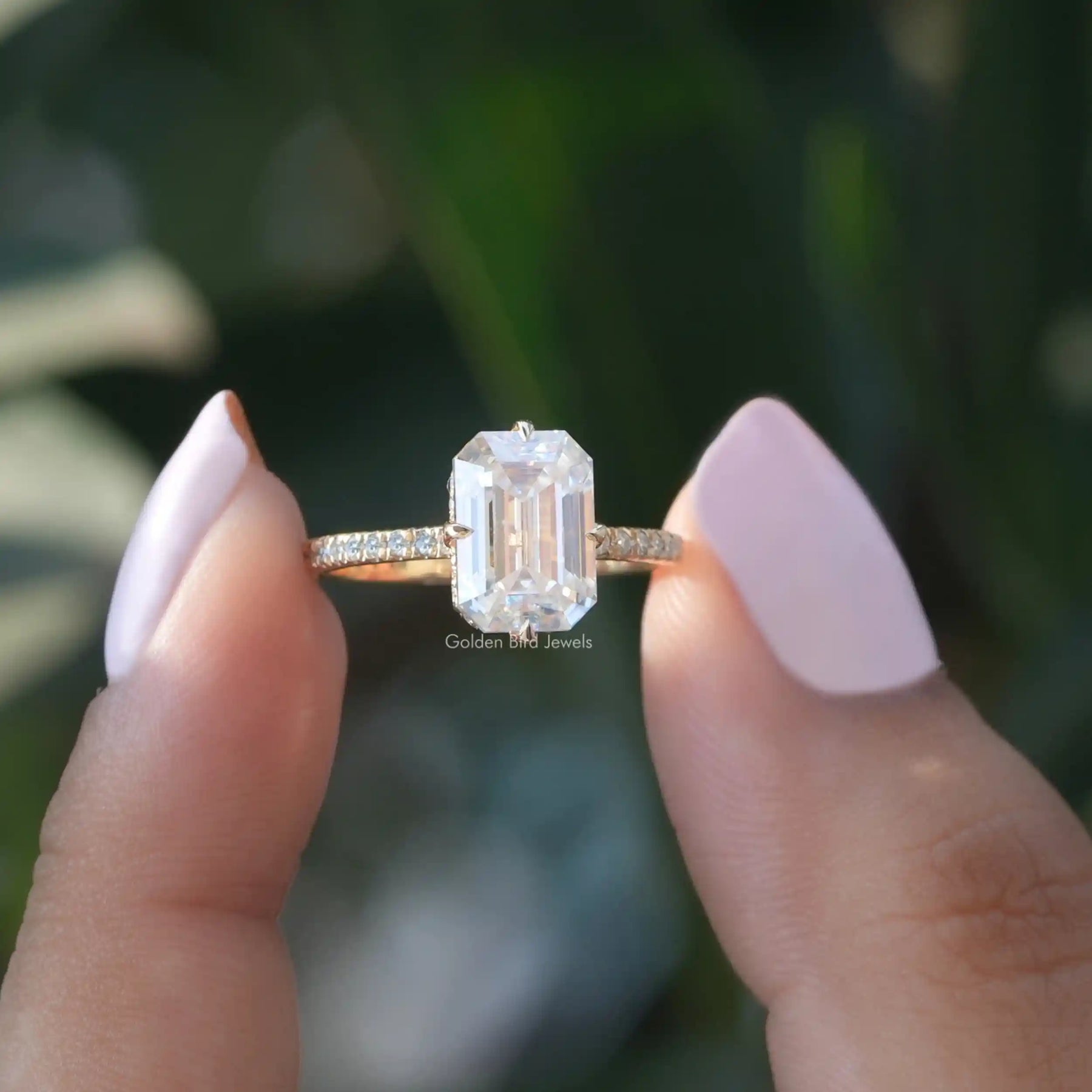 Two fingers holding the Emerald Cut Hidden Halo Engagement Ring