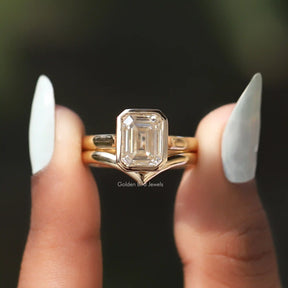 In two finger front view of emerald cut moissanite solitaire bezel set ring