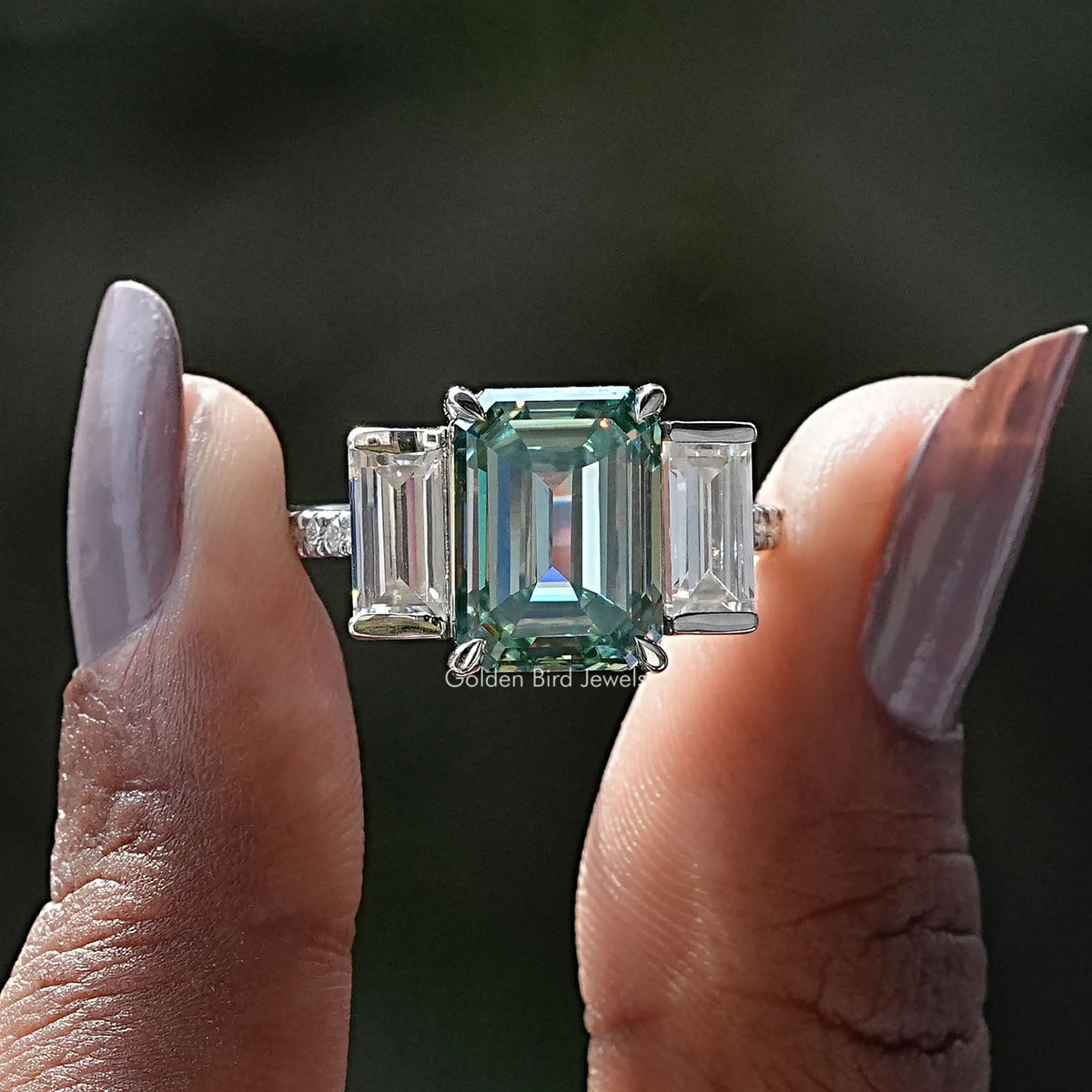 Two fingers holding the Green Emerald Cut Moissanite Ring