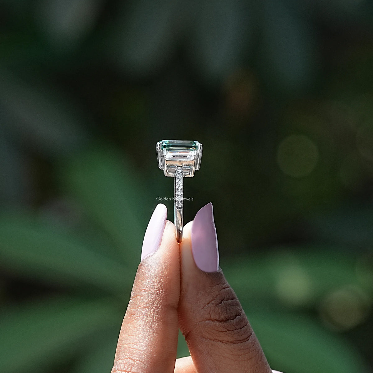 Side View of Emerald And Baguette Cut Moissanite 3 Stone Ring In two fingers