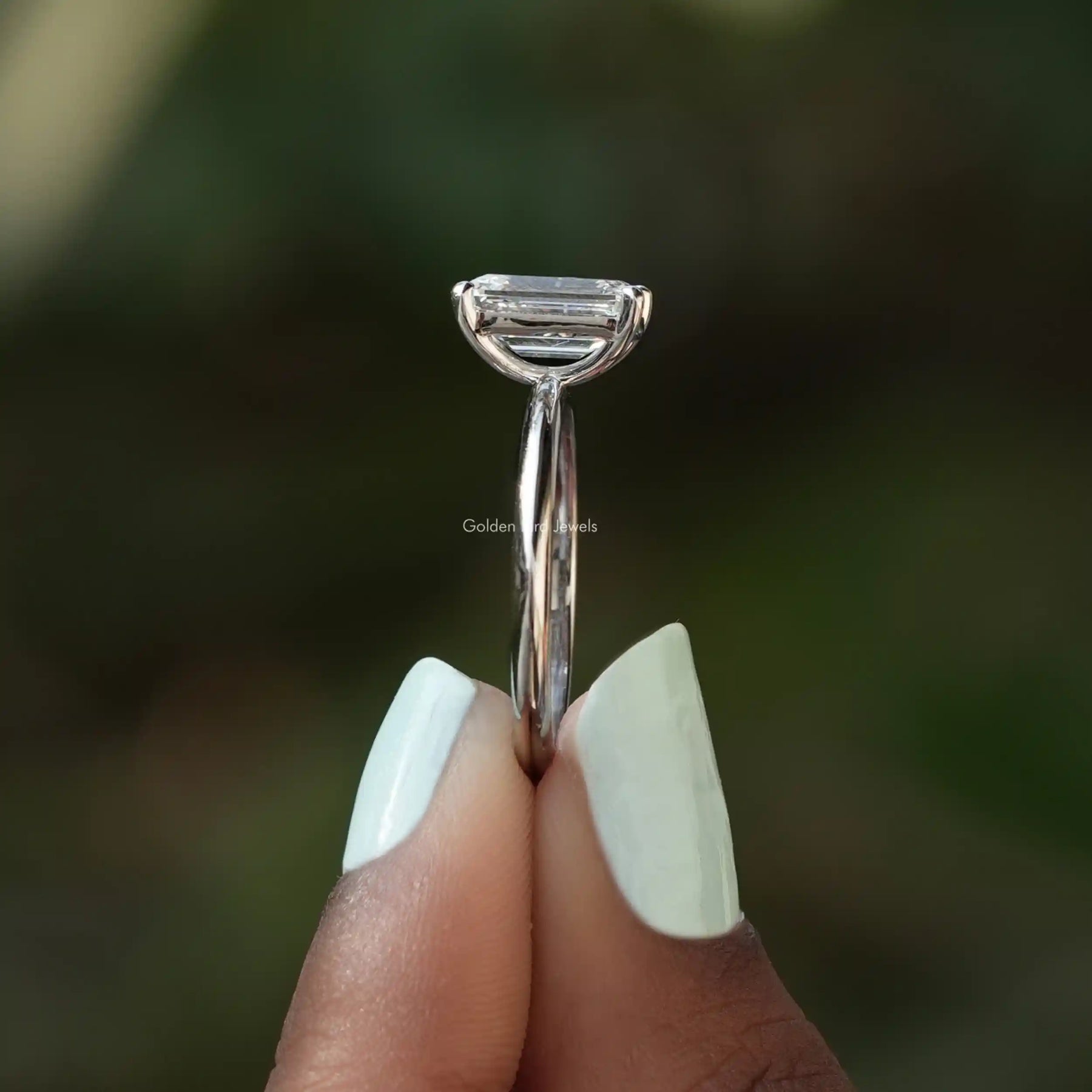 Side View of Emerald Cut Diamond Solitaire Engagement Ring In two fingers