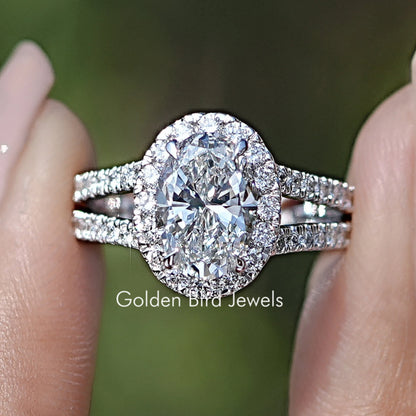 Oval Cut Halo Diamond Split Shank Engagement Ring Held Between Fingers
