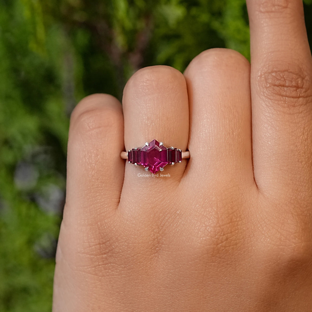 Five-stone ruby red ring on finger with hexagon-cut center and four side stones