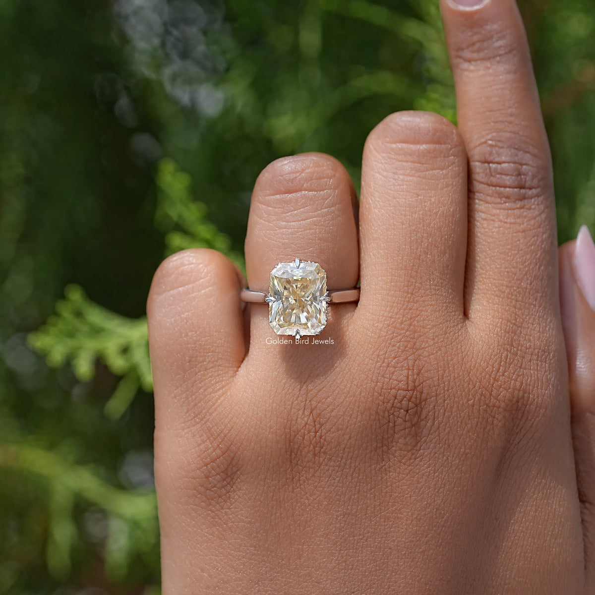 Yellow radiant-cut moissanite engagement ring on finger, square center stone in silver setting