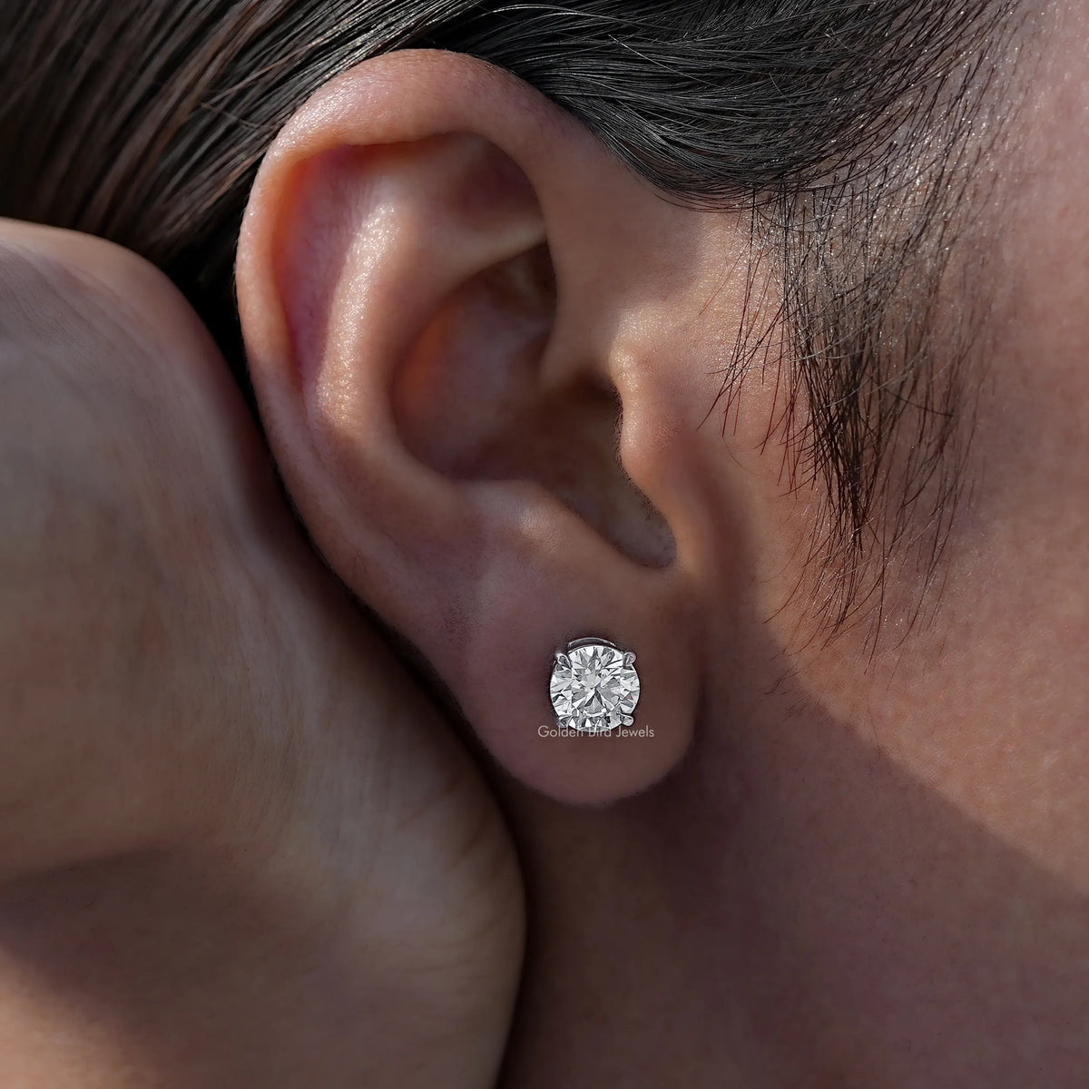 Single round-cut solitaire stud earring on ear with clear gemstone in a silver-toned setting
