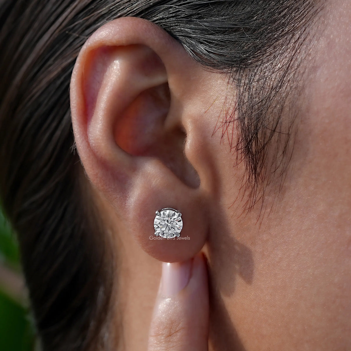 Round-cut solitaire stud earring worn on ear with clear stone and silver-toned bezel