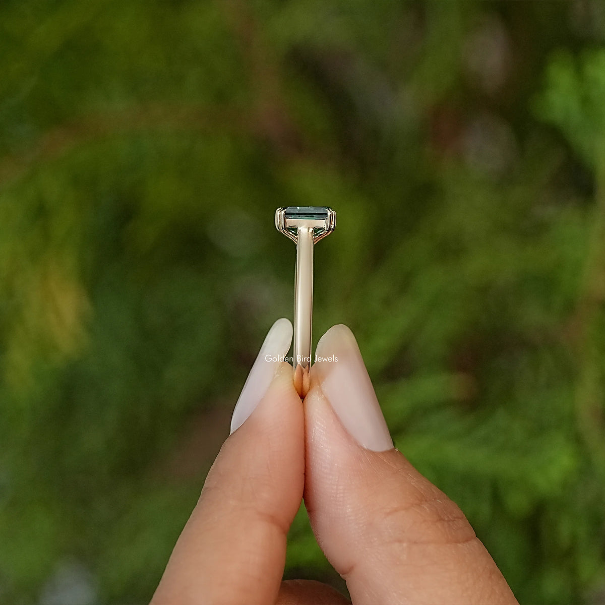 Emerald-cut moissanite engagement ring shown from the side with raised prong setting