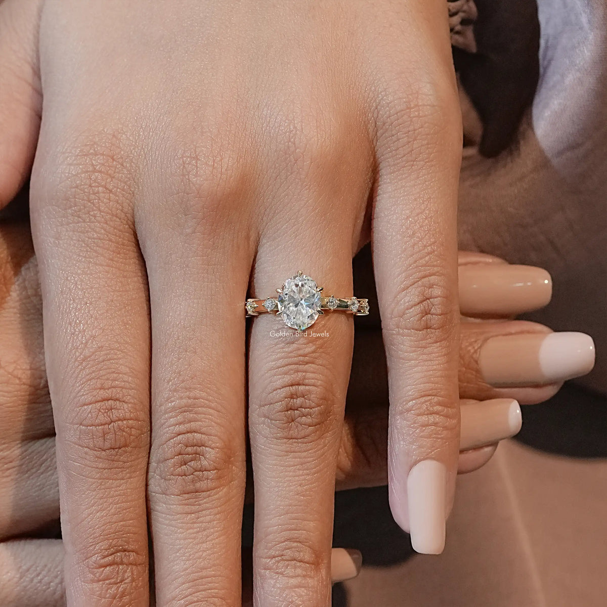 Oval-cut moissanite engagement ring on hand, prong-set center with small side stones