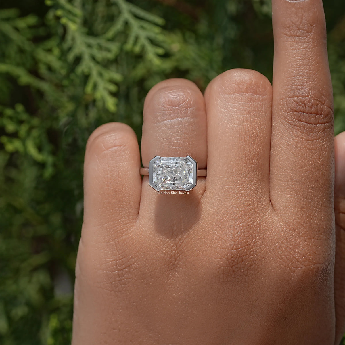Radiant-cut moissanite solitaire ring in silver-tone half-bezel setting on finger