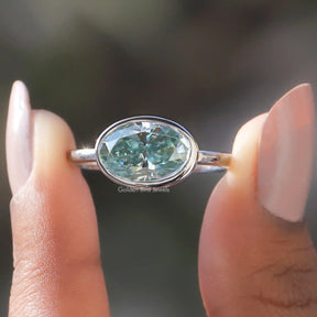 Two fingers holding the Oval Cut East West Bezel Set Solitaire Ring