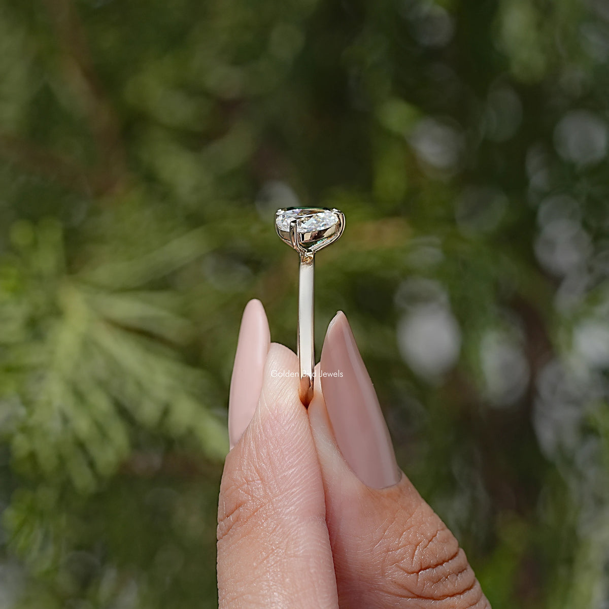 Two-stone ring held up, emerald-cut green and round white stones in prongs