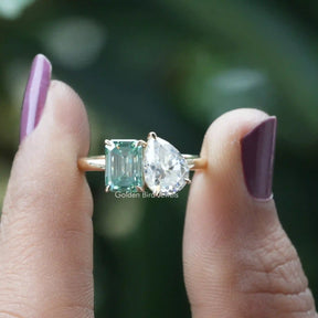 Two-stone pear and emerald cut ring displayed on finger.