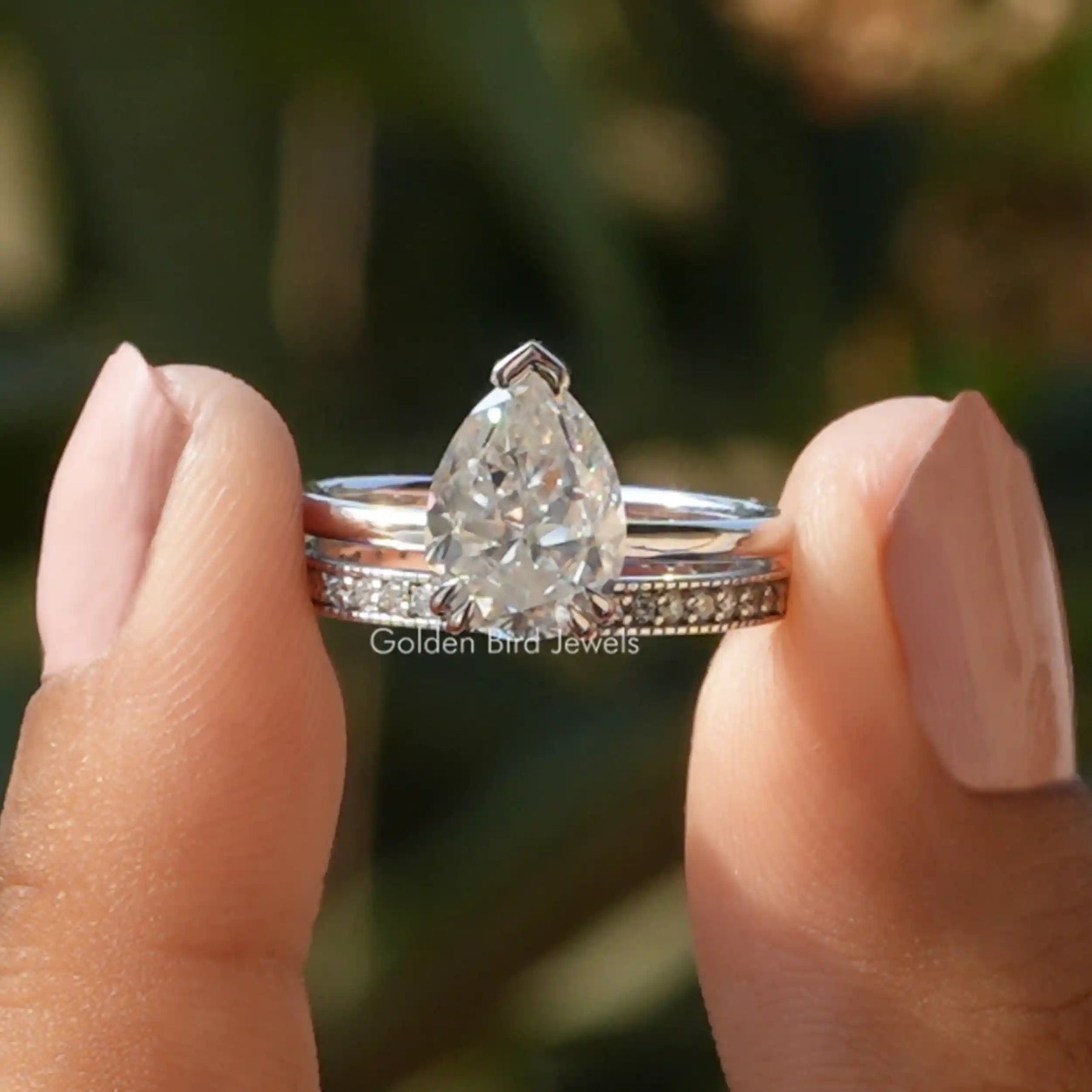 Two fingers holding the Pear Cut Moissanite Hidden Halo Ring