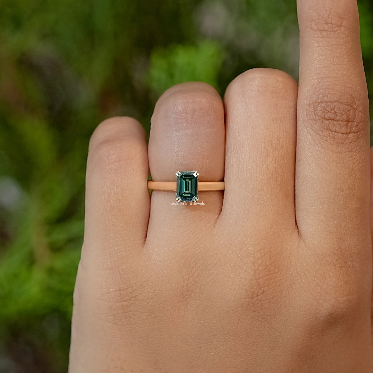 Emerald-cut moissanite ring with dark green center stone on slim band