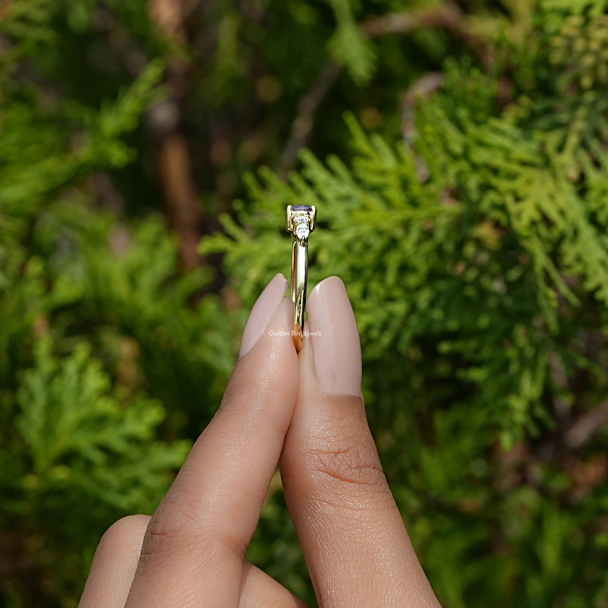 Side View of Round Cut Gemstone Accent Engagement Ring In two fingers