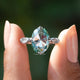 Rose oval cut moissanite accent ring held on two fingers.
