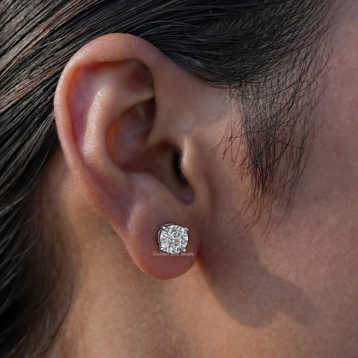 Round-cut solitaire stud earring on ear with a clear gemstone in a silver-toned setting