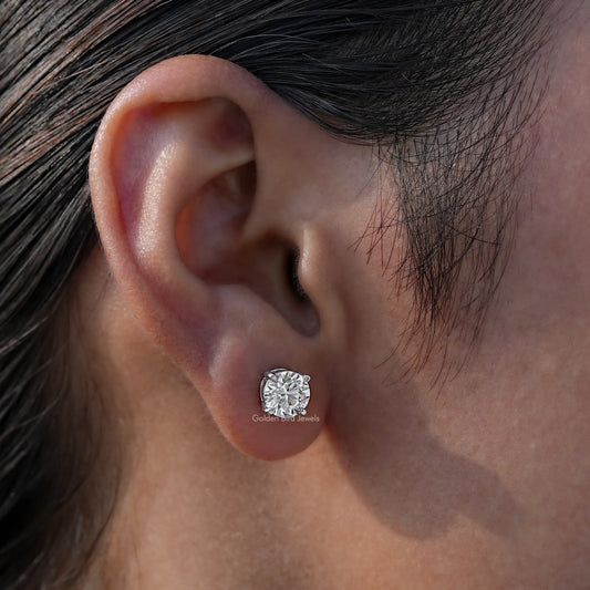 Round-cut solitaire stud earring on ear with a clear gemstone in a silver-toned setting
