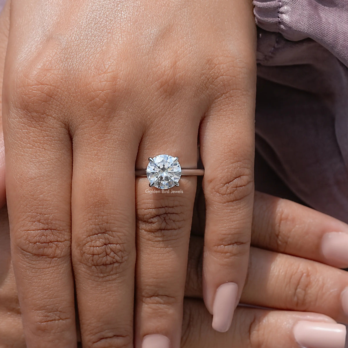 Round solitaire engagement ring worn on finger, round center moissanite with four-prong setting