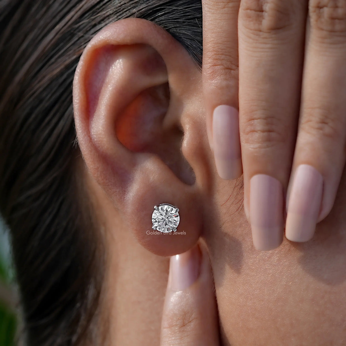 Round-cut solitaire stud earring on ear, with clear stone in silver-toned prongs