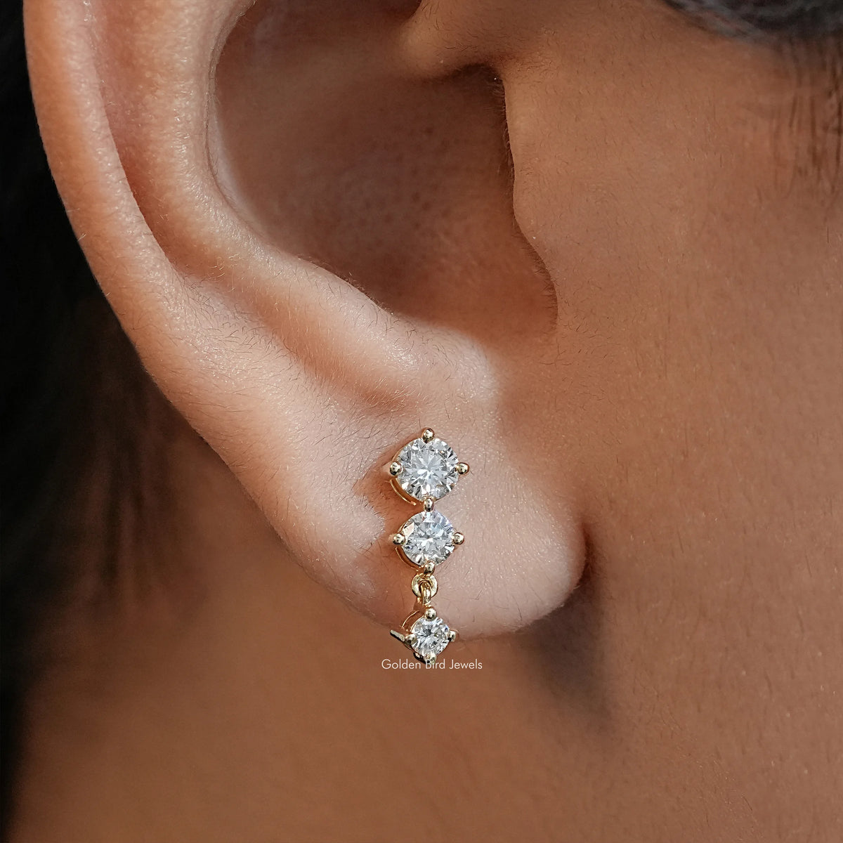 Gold-tone three-stone round diamond stud earring on ear, close-up