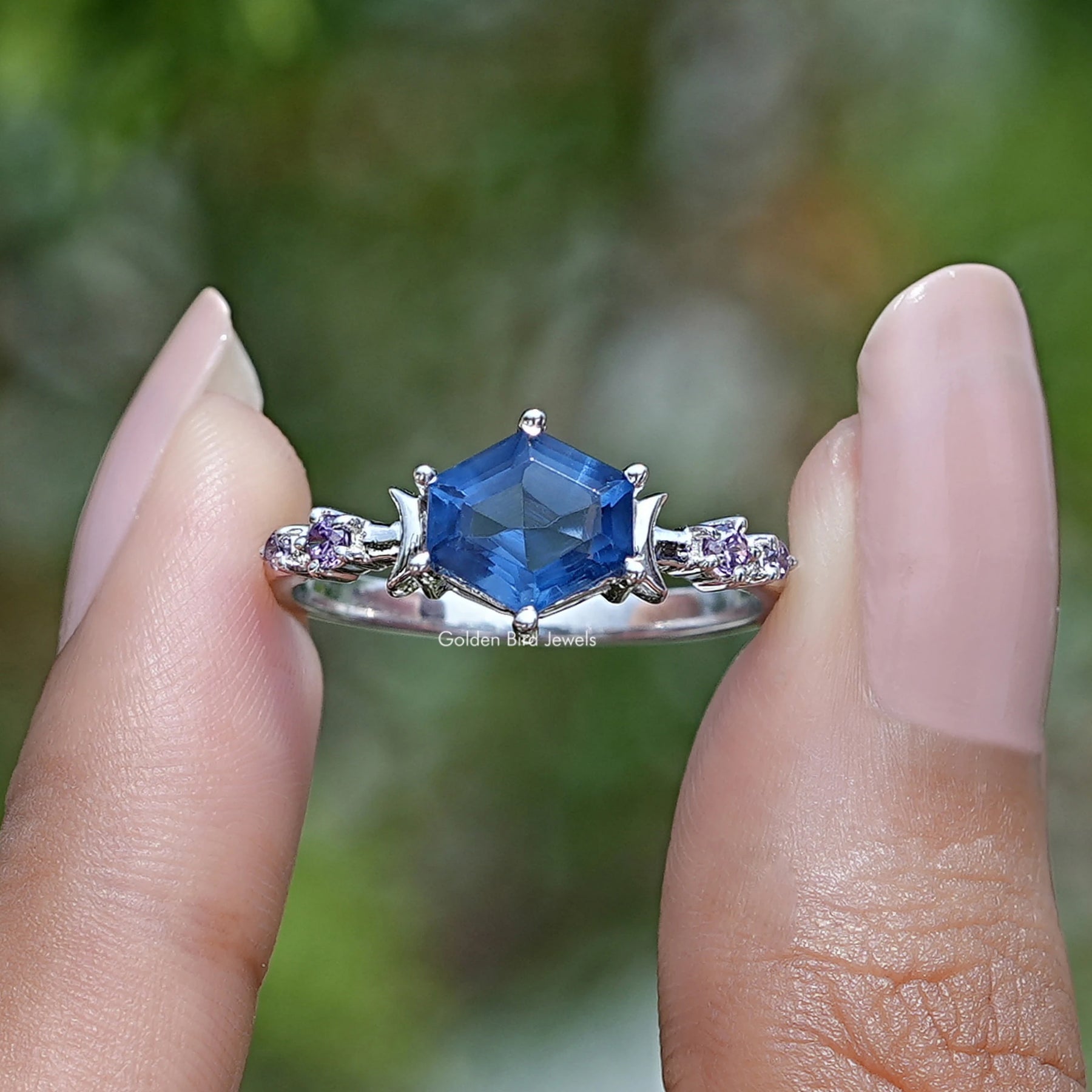 Two fingers holding the Blue Hexagon Cut Engagement Ring