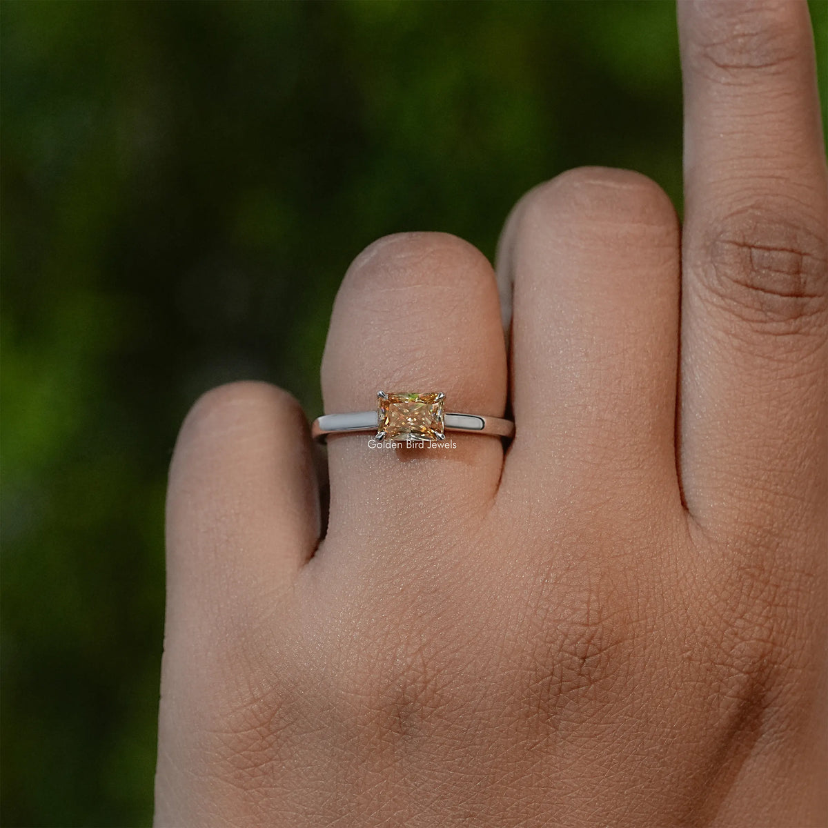 Yellow emerald-cut solitaire ring on silver-tone band, hand-worn side view