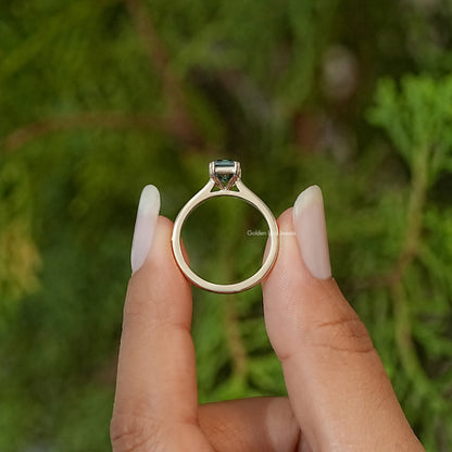 Emerald-cut moissanite ring viewed from front, dark green stone in bezel prongs