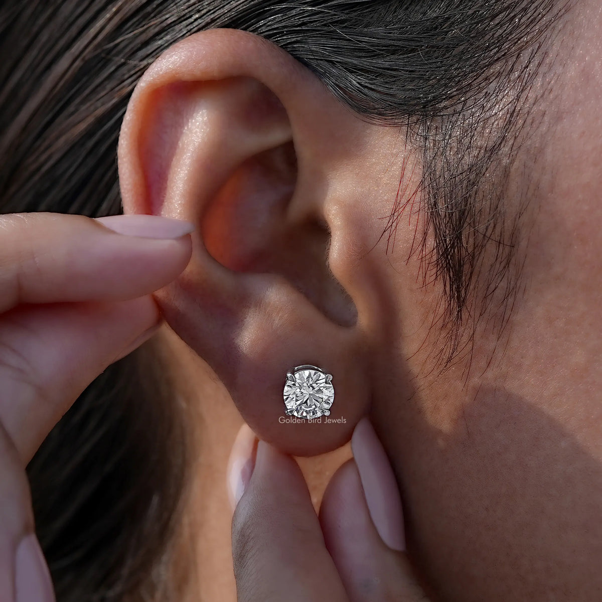 Round-cut solitaire stud earring shown on ear as fingers adjust the earring post
