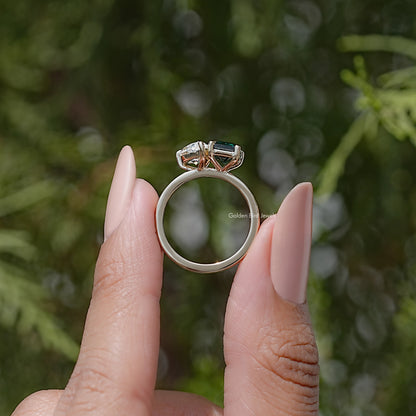 Two-stone ring side view with emerald-cut green and round white stones, band visible
