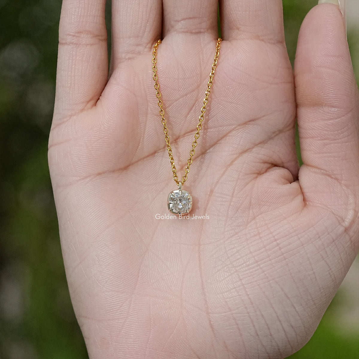 Gold tone necklace pendant with round moissanite solitaire shown in open palm