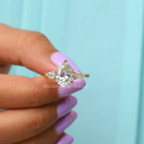 Three-stone  pear moissanite engagement ring holding on two fingers 
